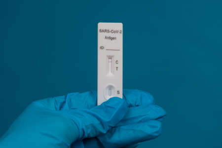 hand in a protective medical glove holds a Negative SARS-CoV-2 Rapid Antigen Test on a blue background.の写真素材
