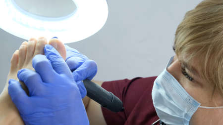 master makes a hardware pedicure to a client in a beauty salon. Peeling feet. Electric pedicure machine. Close up, selective focusの写真素材