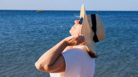 happy 50 year old woman in straw hat and sunglasses enjoying the sun against the blue sea background. Summer, vacation, vacation, active retirees.の写真素材