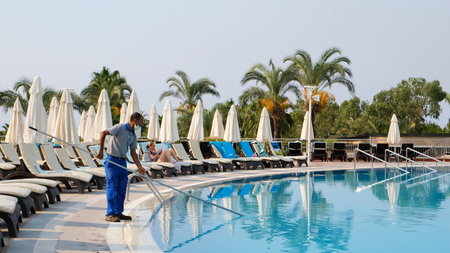 Cleaner of the swimming pool. Man in a blue shirt with cleaning equipment for swimming pools:...