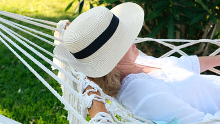 female in a straw hat is resting in a hammock around the palm trees and enjoying the tranquility and relaxation. Vacation concept.の写真素材