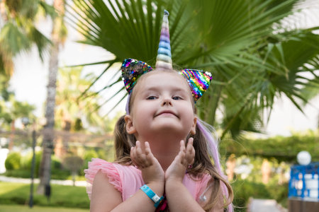 Portrait of a 4 year old girl dressed in a rainbow dress and a unicorn headband against the backdrop...