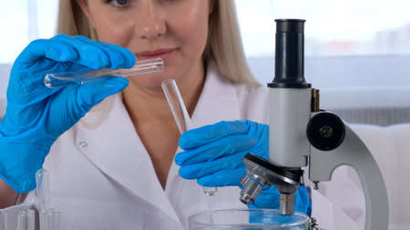 female scientist laboratory assistant in a medical suit and protective gloves conducts research on samples with test tubes for work under a microscope in a laboratory.の写真素材