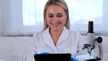 Woman scientist research chemist in a medical suit and protective gloves with a tablet computer and a microscope conducts research in the laboratoryの写真素材