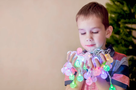 admiration Christmas lights.Christmas foreboding, anticipation of the holiday. boy decorates Christmas tree and holds in hands Christmas lightsの写真素材
