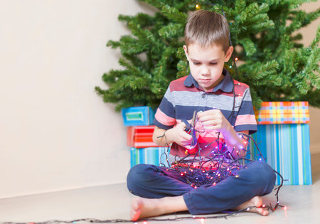 dangerous children antics. curious boy with a pair of scissors in his hand trying dismantle the Christmas lights to see what is insideの写真素材