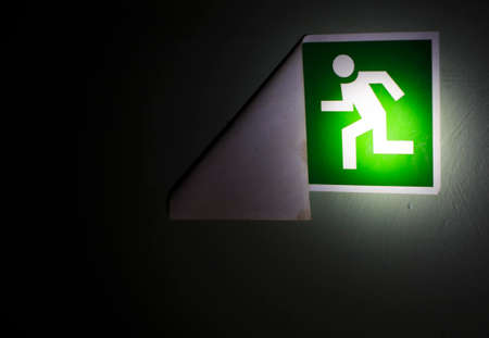 no exit. the concept of finding a way out in the dark. light flashlight illuminates a sign indicating the direction of the exit. but a sign with a picture of the running man has come unstuck from the wall and the direction arrow is not visible.の写真素材