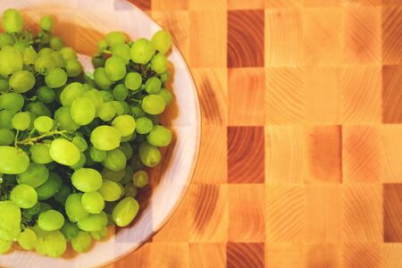 Fresh green grape on the plate on the wooden cutting board, top viewの写真素材