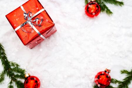 Christmas gift box and holiday decor with fir tree brunch and red balls. Snowy picture. New year decoration background on the artificial snow, flat lay, top view, horizontal, copy spaceの写真素材