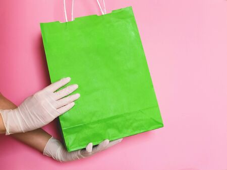 Consumer pack product. Delivery. Hand in a glove holds a green craft package with handles. Space for logo.の写真素材