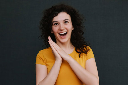 Portrait of funny emotional curly girl on grey background. Surprise. Joy. Happy.