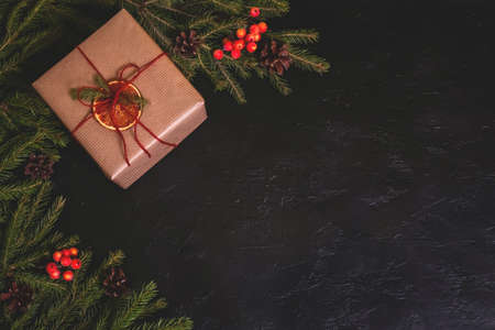 Christmas composition. Handmade gift box decorated with craft paper with brunches on dark background. Copy spaceの写真素材