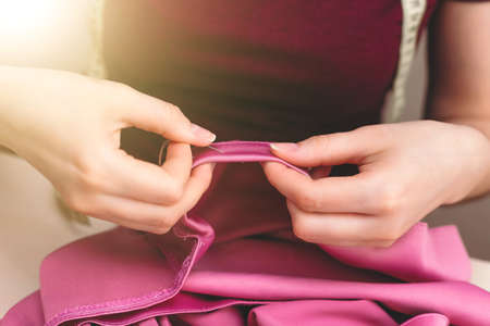 Happy attractive young woman seamstress sitting and sews on sewing machine on light background. Concept of sewing, handmade goods. Advertising of studio. Sunlightの写真素材
