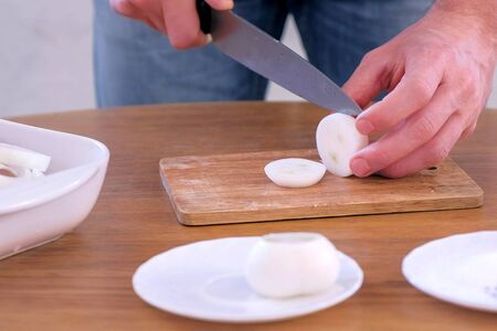 Man cutting onion on rings and put to pieces pork meat shashlik to marinate, hands closeup. Preparing cooking fresh pork to barbeque and grilling, cutting on wooden board on kitchen table.の写真素材