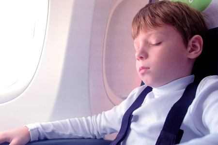 Boy sleeps on a plane next to the window. Side view