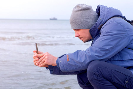 Making content for blog, modern freedom work. Man tourist traveller blogger in winter clothes at sea...