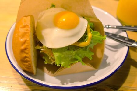 Big Burger with egg and fresh vegetables serve on the plate with fork and knife. Harmful and appetizing fast food food in fast food restaurant.の写真素材