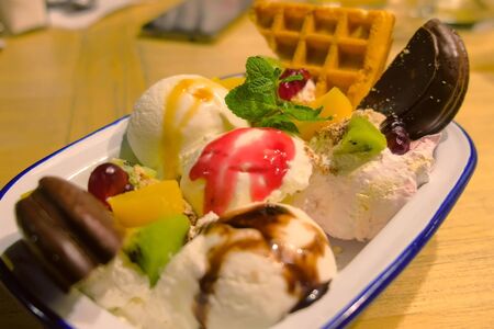 Sweet dessert with ice cream, cookies, waffles and fruits in a white plate in cafe, closeup view.の写真素材