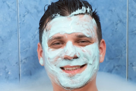 Portrait of smiling young man with alginate mask lying in bathroom with foam at home. Spa beauty treatment. Man wellness, skincare and self love concept. Relaxing and enjoying his time.の写真素材