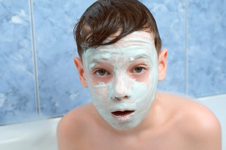Surprised face of child teen boy with alginate mask in bathroom at home. Spa beauty treatment. Teen problem skin, wellness, skincare and self love concept. Relaxing and enjoying his time.の写真素材
