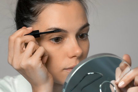 Woman is applying fixing gel on eyebrows using brush looking at mirror, closeup face. Beauty procedure at home. Modern trendy styling, correction, coloring of eyebrows.の写真素材