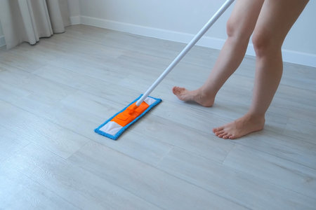 Woman is cleaning and mopping the linoleum floor using mop in living room, legs close-up. Housekeeping, housework, household duties concept. Modern interior of the flat.の写真素材