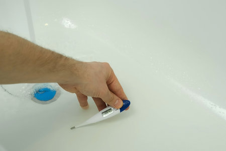 Closeup footage of man's hand using thermometer to check water temperature in bath. Man is preparing a hot water to take a bath. He wants to relax after busy day.の写真素材