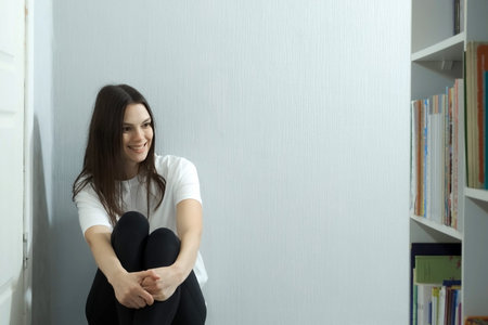 Young woman is sitting near bookcase and looking at her books. She is enjoying her books. The problem of hoarding and junk in modern life.の写真素材