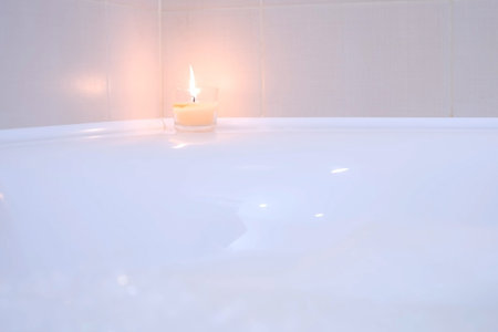 Prepared bath with foam and burning candle for relaxation at home, close-up view. Decorated bathroom...
