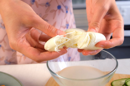 Woman hands rips large piece of mozzarella cheese into parts on kitchen at home. Cooking Italian food, dish. Tasty delicious meal. Fresh ingredient, preparing delicacy.の写真素材