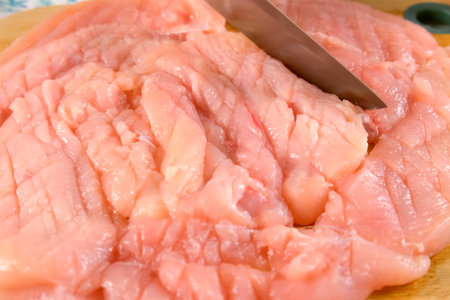 Woman hands cutting chicken breast on slices to cook on kitchen at home. Preparing making cuts on chicken fillet. Ingredient recipe cuisine culinary. Homemade healthy meal. Protein nutrition.の写真素材