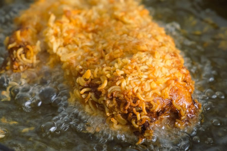 Breaded in dry noodle chicken breast frying in hot oil in pan on stove. Female chef cooking poultry...