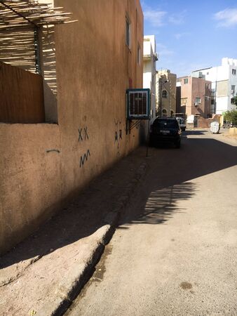 The street of the Arab city where people live. Near the house there is a car behind the trash can is visible. On the wall of the house is a drawing and an inscription. Jordan, Aqaba.のeditorial素材