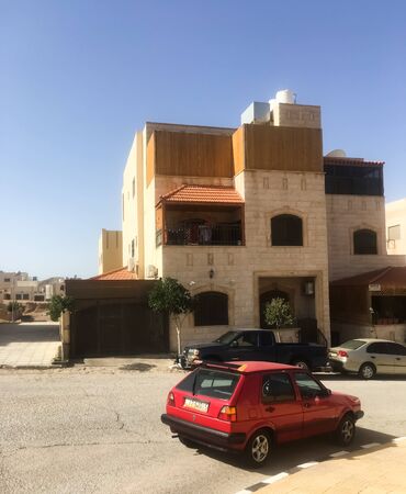 A red car parked on the street along the road opposite the house. A residential building on the balcony is drying things. Jordan, Aqaba. Turizm.のeditorial素材
