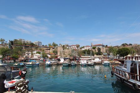 View of the fortress and boats in the port of the old city of Antalya. Tourist boats in the port. People are sitting on the beach with beer.のeditorial素材