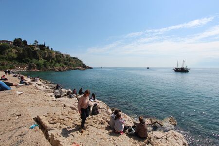 People sits along the coast and look at the Mediterranean sea. Tourist port. A tourist ship is sailing on the sea. Turkey, Antalya.のeditorial素材