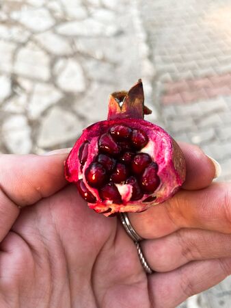 In a female hand, a small pomegranate with seeds on the background of paving slabs. Place for text.の写真素材