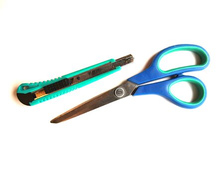 Blue scissors and a green stationery knife on a white isolated background. Place for text. View from above.の写真素材
