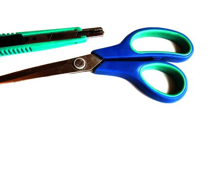 Blue scissors and a green stationery knife on a white isolated background. Place for text. View from above.の写真素材