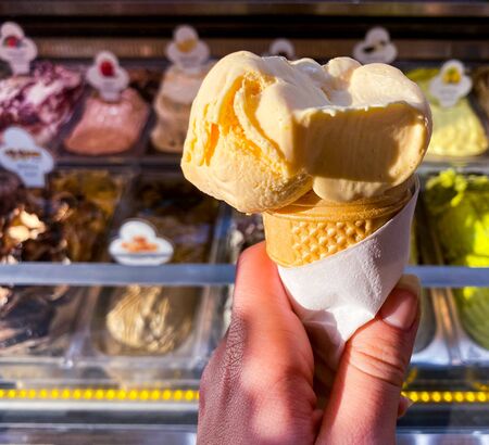 In a female hand, yellow ice cream on a background of a counter with ice cream. Place for text. Travels.の写真素材