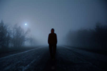 A photograph in a dark exposure of a guy standing in the fog on a deserted roadの写真素材