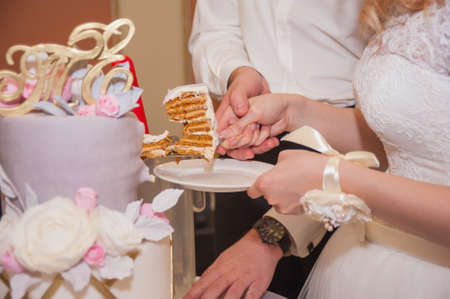 The bride and groom cut the wedding cake together and put on the first braidの写真素材