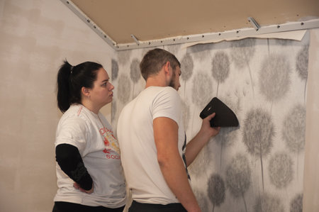 A young family, a guy and a girl are making repairs together, gluing wallpaper and painting the wallsの写真素材