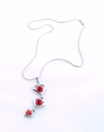 Silver chain and pendant with hearts, red roses and crystal on light background.の写真素材