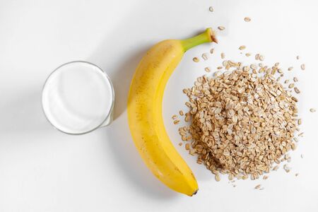 a glass of milk on a white table, oatmeal and a bananaの写真素材