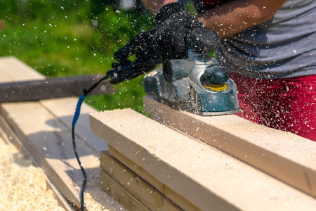 man planning boards with electric tools, chips flying in all directions. Construction, wood...