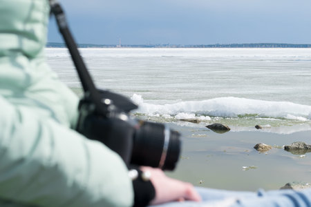 in the winter, in the offseason, the girl sits on the coast on the background of the icy lake