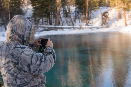 man taking pictures on a smartphone lakeの写真素材