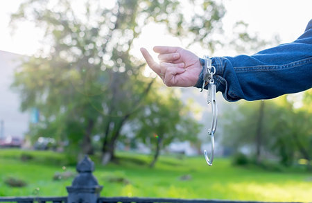 hand of man, in handcuffs shows middle finger, fuck, on the street