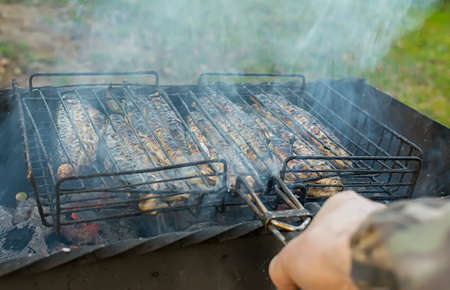 hand of a man holding a grill with fried fishの写真素材